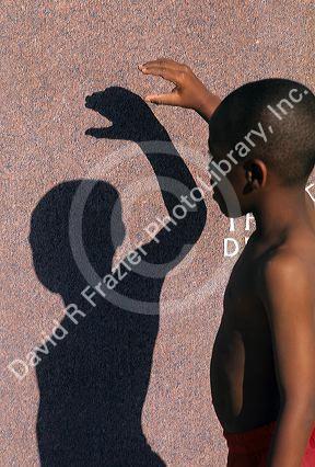 An african american boy makes a shadow puppet on a wall.