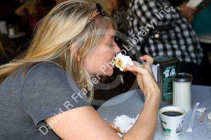 Woman eating a beignet at Cafe Du Monde in the French Quarter of New Orleans, Louisiana, USA.