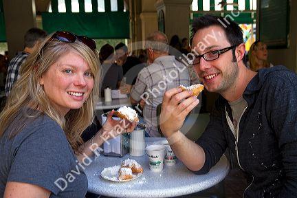 A couple eating beignets at Cafe Du Monde in the French Quarter of New Orleans, Louisiana, USA.