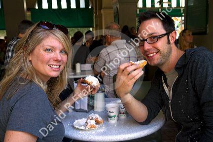 A couple eating beignets at Cafe Du Monde in the French Quarter of New Orleans, Louisiana, USA.
