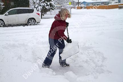 Woman shoveling winter snow off of a sidewalk in Boise, Idaho, USA.