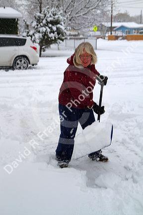 Woman shoveling winter snow off of a sidewalk in Boise, Idaho, USA.