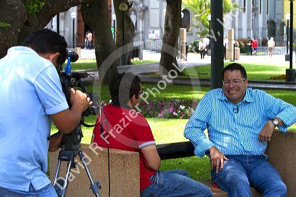 Television camera recording men having an interview in Central Park of the Miraflores district of Lima, Peru.