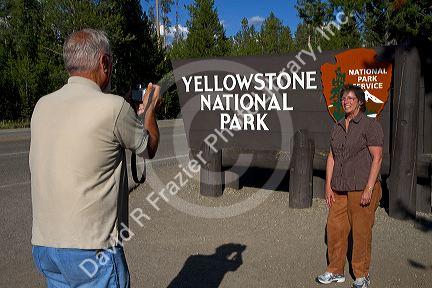 Tourists take a photo in front of the Yellowstone National Park entrance sign, West Yellowstone, Montana, USA.