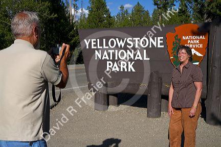 Tourists take a photo in front of the Yellowstone National Park entrance sign, West Yellowstone, Montana, USA.