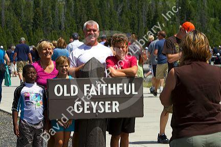 Tourists pose for a photo at Old Faithful geyser in Yellowstone National Park, Wyoming, USA.