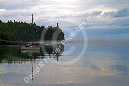 A morning view of Spilt Rock Lighthouse with sailboat and mist on Lake Superior, Minnesota, USA.
