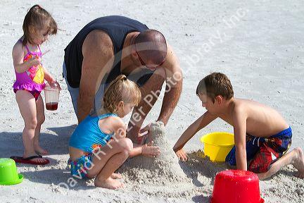 Father helping children build a sand castle at Madeira Beach in Pinellas County, Florida, USA.