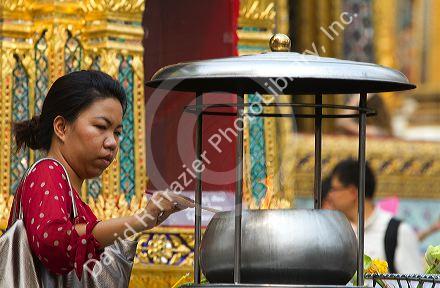 Woman lighting incense at the Temple of the Emerald Buddha located within the precincts of the Grand Palace, Bangkok, Thailand.