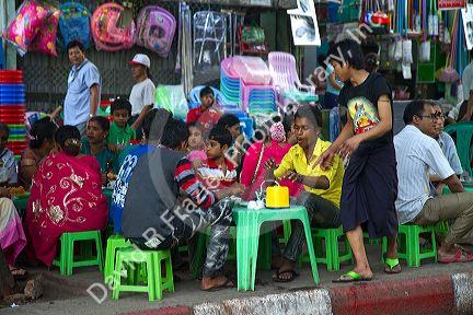 Burmese people eat and drink at small tables and chairs outdoors in (Rangoon) Yangon, (Burma) Myanmar.