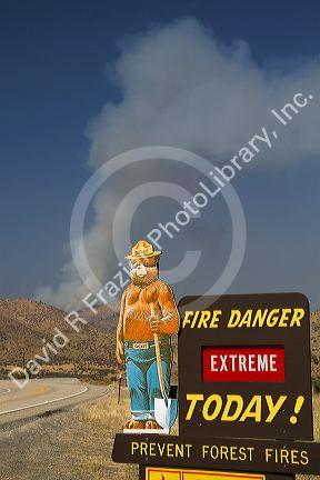 Smokey Bear extreme fire danger sign with a plume of smoke from a forest fire in the back ground in Boise County, Idaho, USA.
