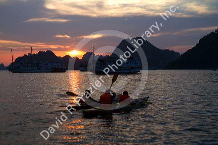 Tourists using sea kayaks at sunset in Ha Long Bay, Vietnam.
