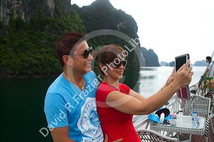 Vietnamese tourists taking a selfie aboard a tour boat in Ha Long Bay, Vietnam.