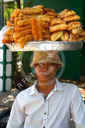 Vietnamese street vendor balances baked sweet snacks on his head in Nha Trang, Vietnam.
