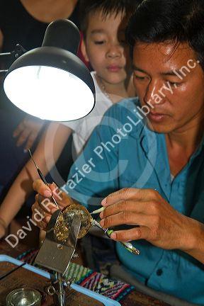 Worker on a pearl farm placing sand in an oyster shell to grow a cultured pearl, Ha Long Bay, Vietnam.