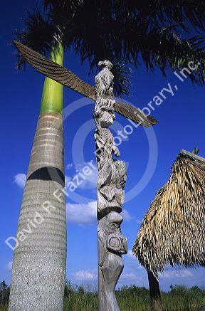 Totem pole with palm tree and chopekcheke. A traditional Seminole Miccosukee Indian dwelling.