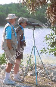 Senior citizens looking through spotting scopes at the J.H. Ding Darling National Wildlife Refuge on Sanibel Island, Florida.  Man is a volunteer at the refuge.