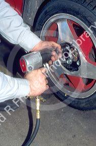 An auto mechanic using an impact wrench to change car tire and wheel.