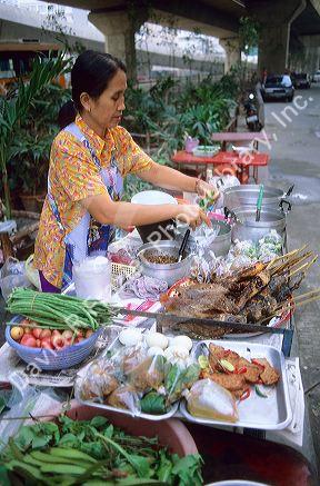 Thai woman cooking food at street vendor stall in Bangkok Thailand.