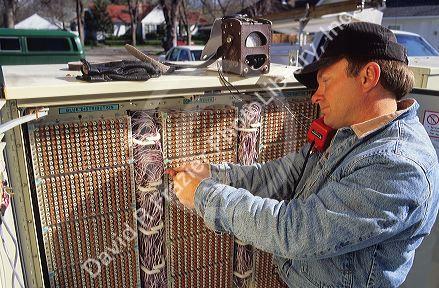 Telephone installer working with circuit box outdoors.