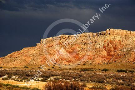 Butte along US highway 550 near Bernalillo, New Mexico with dark storm cloud backdrop in the evening sun.