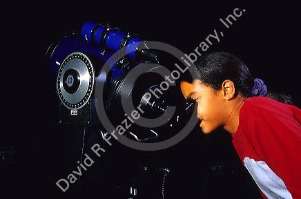 A sixth grade female student looks through a telescope.