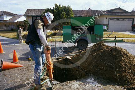 Worker with protective gear uses a jackhammer.