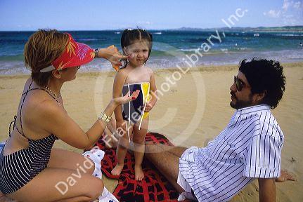 Hispanic family at the beach. Parents apply sunscreen to childs face.