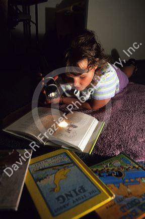 A young girl reading a book with a flashlight.