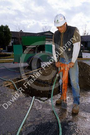 Worker with protective gear uses a jackhammer.
