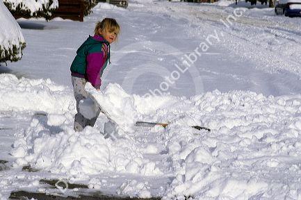 Young girl wearing winter coat shovels snow from the sidewalk.