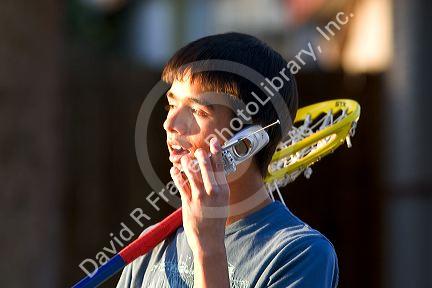 Teen lacrosse player using a cell phone.