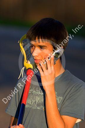 Teen lacrosse player using a cell phone.