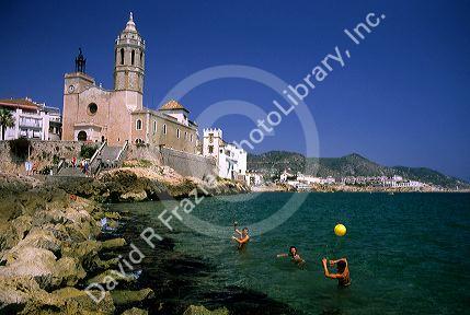 Young people play in the sea in front of a Catholic church in Sitges, Spain.