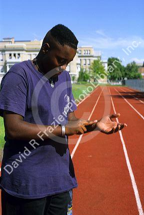 An african american teenage boy checking his pulse with two fingers on his wrist.