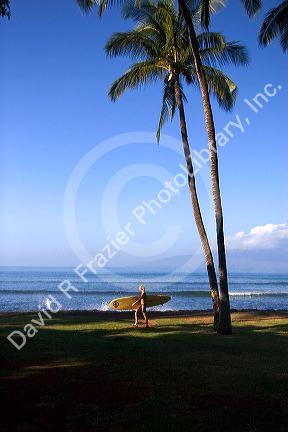 Girl walking with surfboard on the island of Maui, Hawaii.