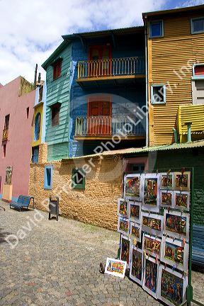 Paintings being sold on Caminito street in front of colorful buildings in the La Boca area of Buenos Aires, Argentina.