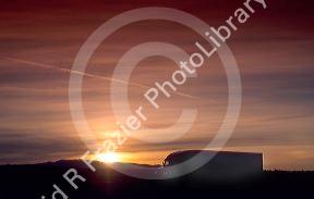 Long haul truck driving on highway at sunset.