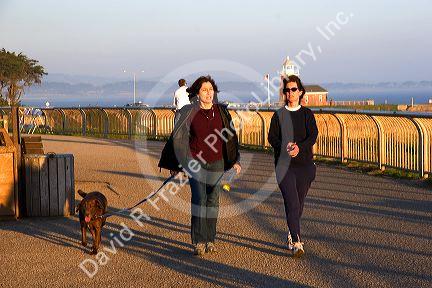 Women walking a dog with red brick lighthouse in the background at Santa Cruz, California.