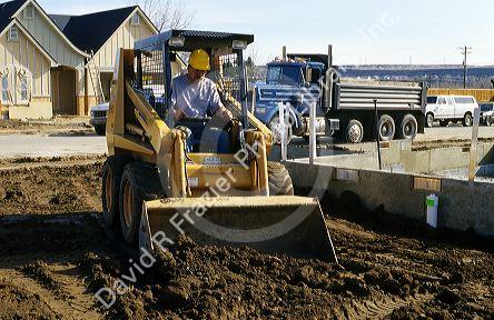 Construction worker using a bobcat type loader to backfill a foundation in Boise, Idaho.