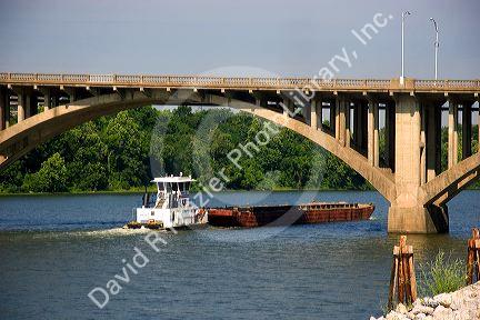 Tug boat and river barge pass under a bridge over the Arkansas River in Little Rock, Arkansas.