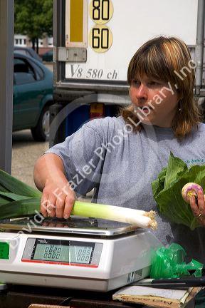 A woman weighs leeks at an open air market in Neuf-Brisach, France.