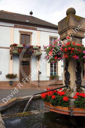 Water fountain with red geraniums in the village of Roschwihr, Eastern France.