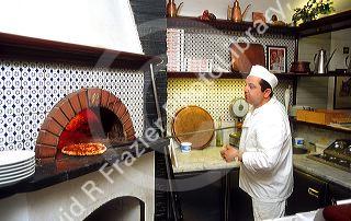 Pizza chef in Santa Margherita, Italy inserts pie into wood fired oven.