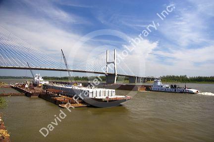 A tugboat and barge on the Mississippi River cross under a modern suspension bridge at Cape Girardeau, Missouri.