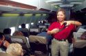 Asian female flight attendent holding a seat belt buckle, conducts a safety briefing before takeoff.