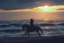 Woman riding a horse along the beach at sunset in Washington state.