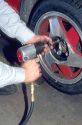 An auto mechanic using an impact wrench to change car tire and wheel.