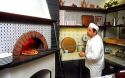 Pizza chef in Santa Margherita, Italy inserts pie into wood fired oven.