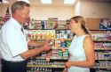 Woman consulting pharmacist about vitamins in a supermarket pharmacy.